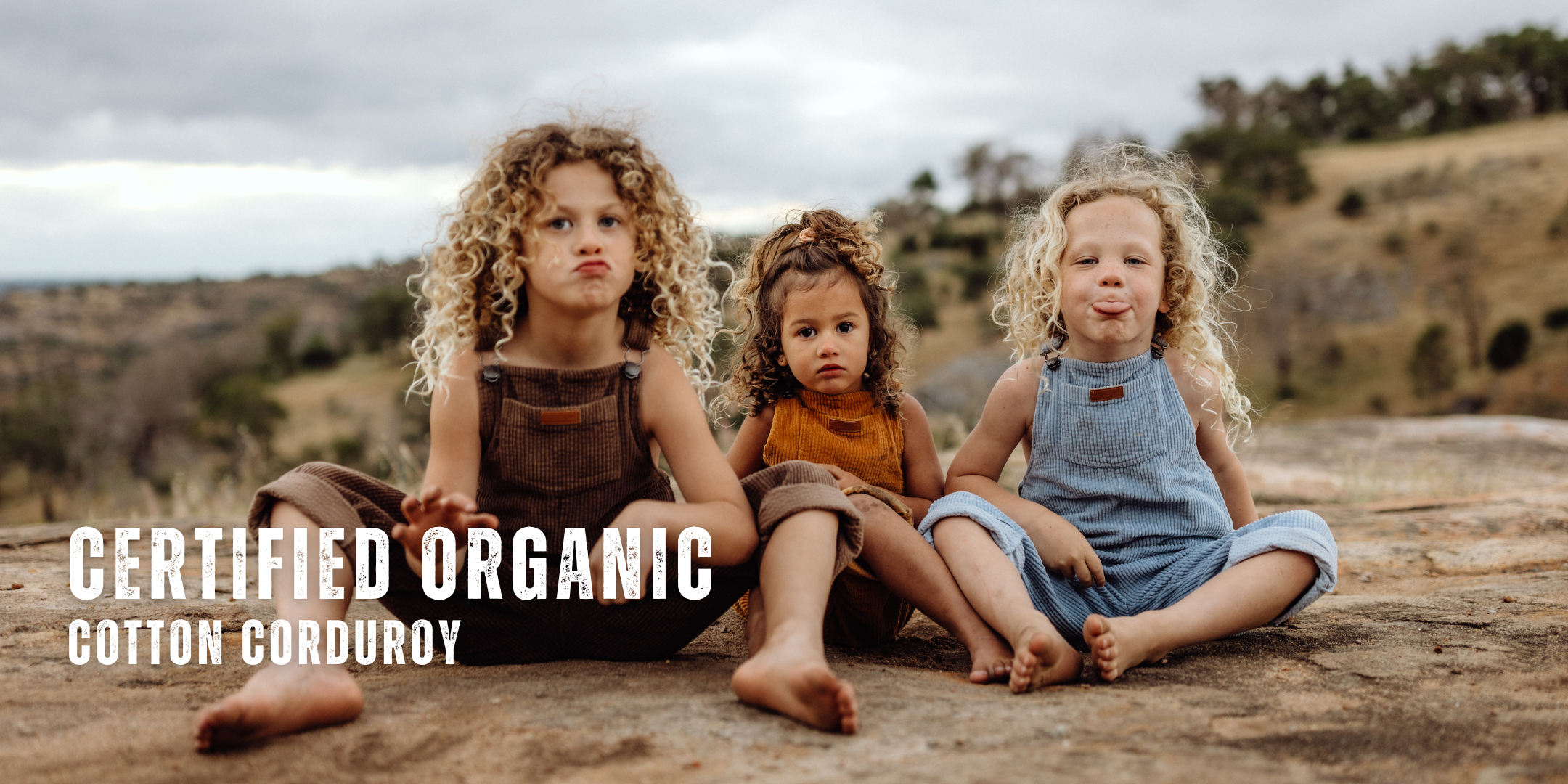 organic cotton corduroy overalls, dungarees for infants,toddler & kids in orange, blue & brown. 3 Kids are sitting on a rock wearing the overalls homepage banner