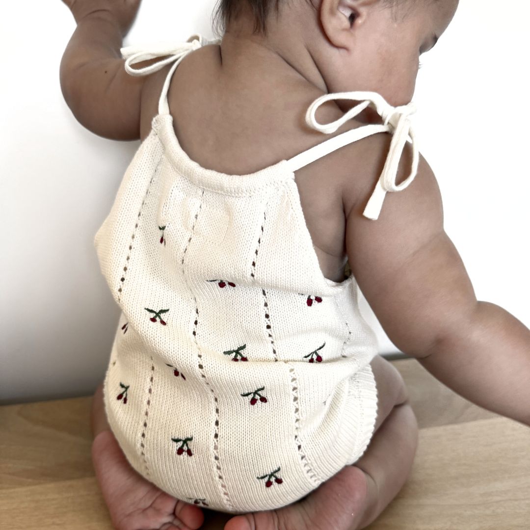 organic cotton romper for babies ages 0 - 24 months. Croquet style romper in beige with Cherry embroided into it back view sitting down