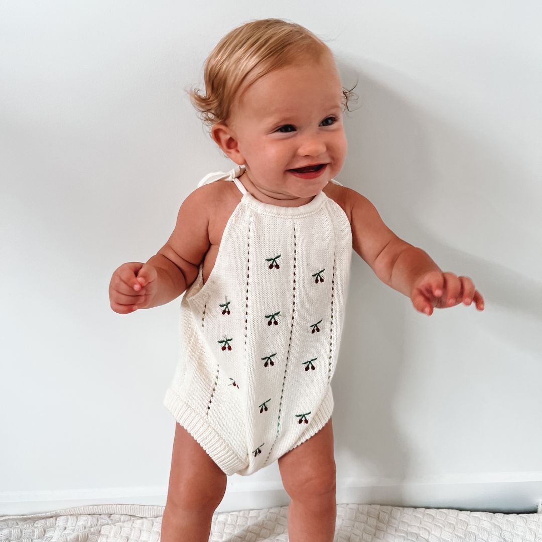 organic cotton romper for babies ages 0 - 24 months. Croquet style romper in beige with Cherry embroided into it standing front view
