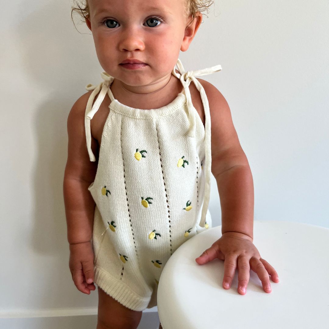 organic cotton romper for babies ages 0 - 24 months. Croquet style romper in beige with lemons embroided into it standing front view