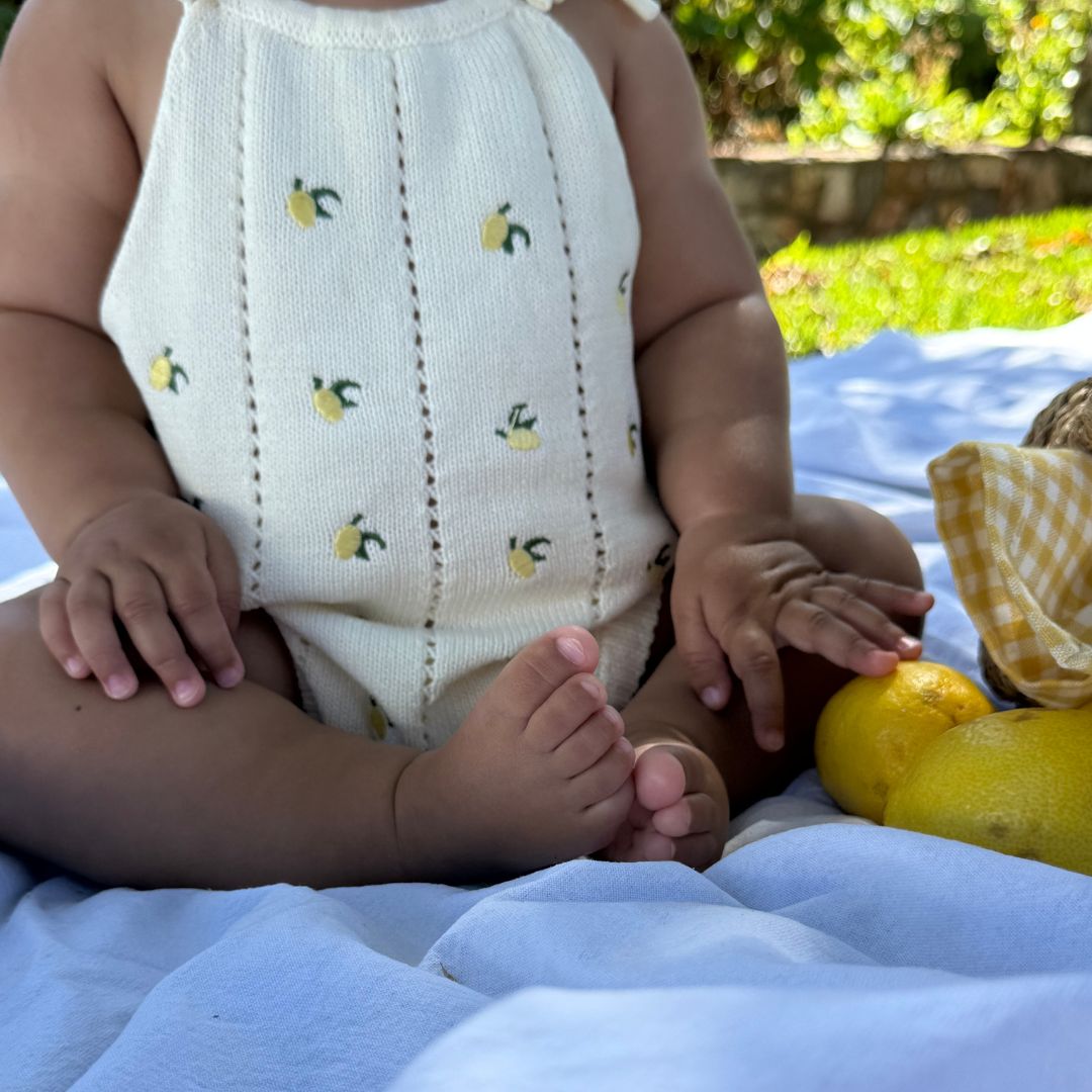organic cotton romper for babies ages 0 - 24 months. Croquet style romper in beige with lemons embroided into it standing front view sitting down