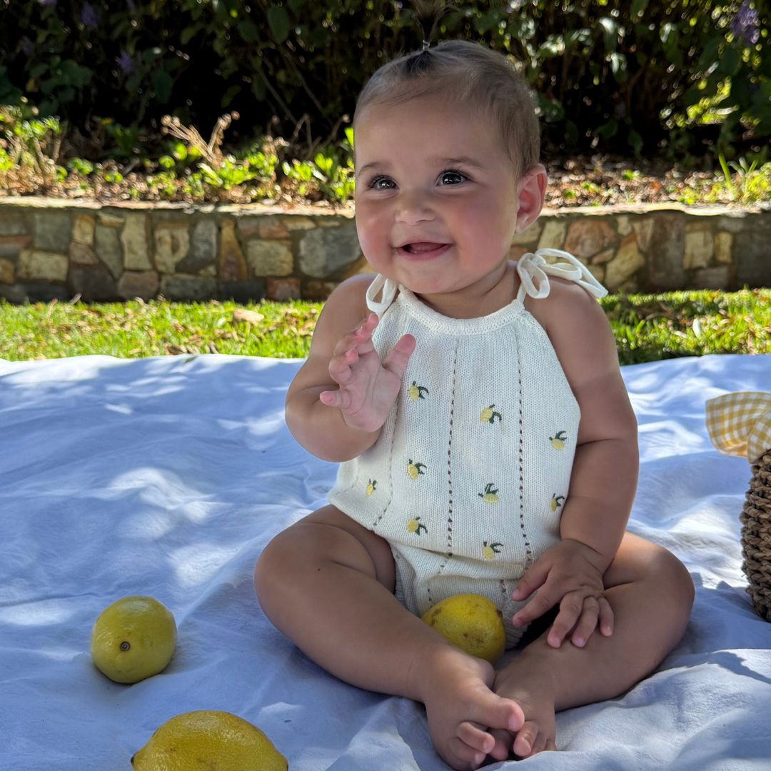 organic cotton romper for babies ages 0 - 24 months. Croquet style romper in beige with lemons embroided into it standing front view sitting down showing whole garment