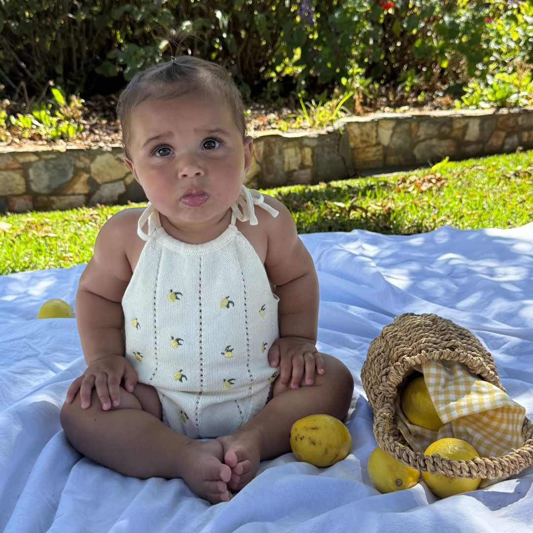 organic cotton romper for babies ages 0 - 24 months. Croquet style romper in beige with lemons embroided into it standing front view sitting down showing whole garment legs together