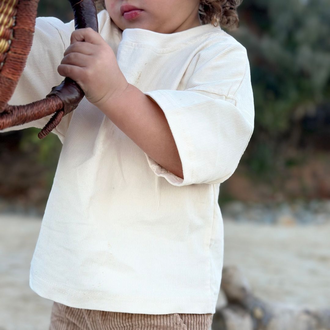 young boy holding a basked wearing kids beige corduroy loose t-shirt and shorts on a beach