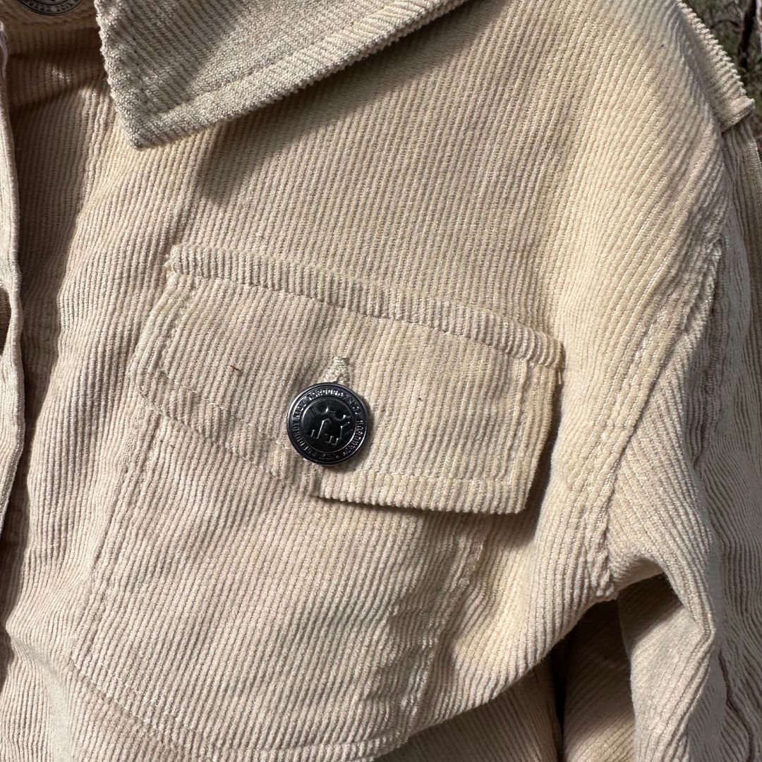 close up of Kids and toddlers organic corduroy long sleeve dress shirt in coconut showing the detail of the garment and engraved branded logo on button