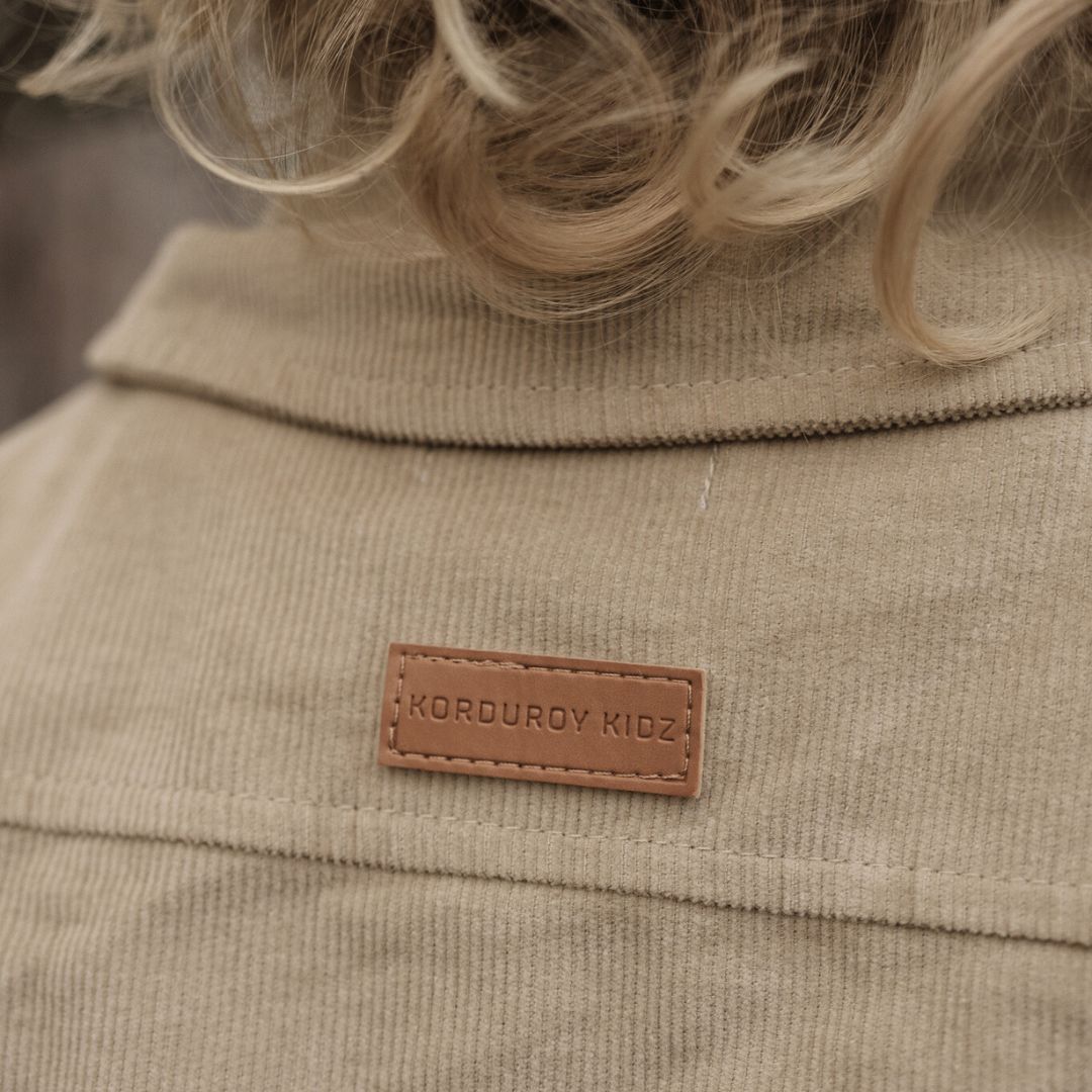 kids organic corduroy long sleeve dress shirt in coconut close up showing PU leather engraved logo of korduroy kidz