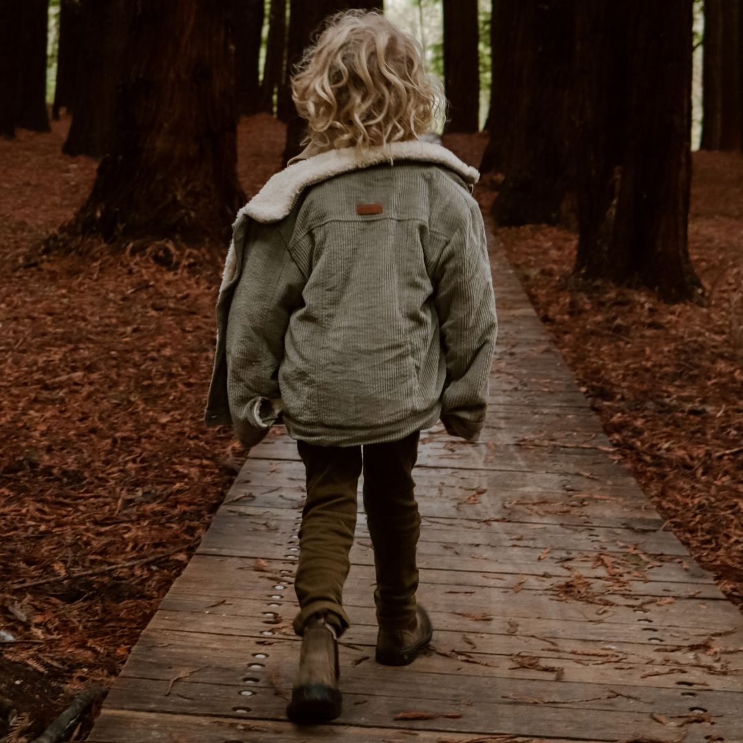 Kids and toddlers organic corduroy sherpa fleece jacket in sage walking on a boardwalk situated around nature